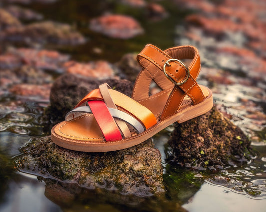 A stylish sandal sits on a rock in water.