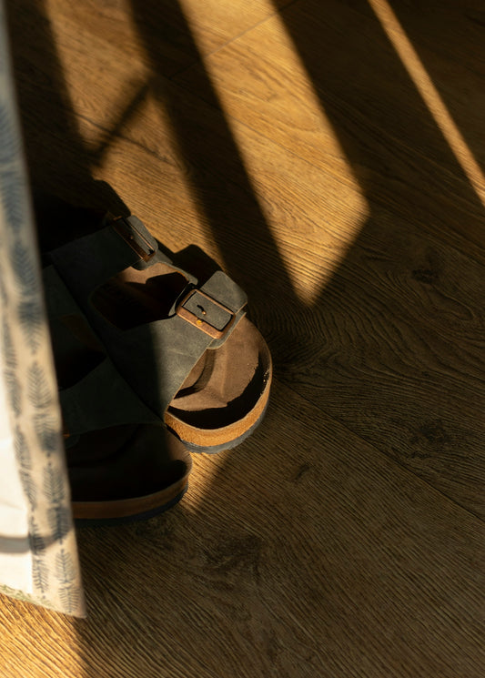 Sandals sit on a wooden floor with sunbeams.