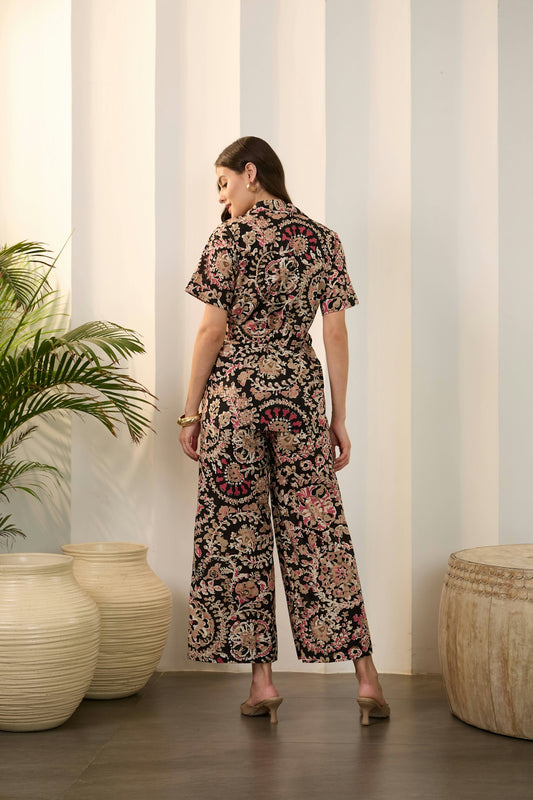 Woman in a patterned jumpsuit standing indoors.