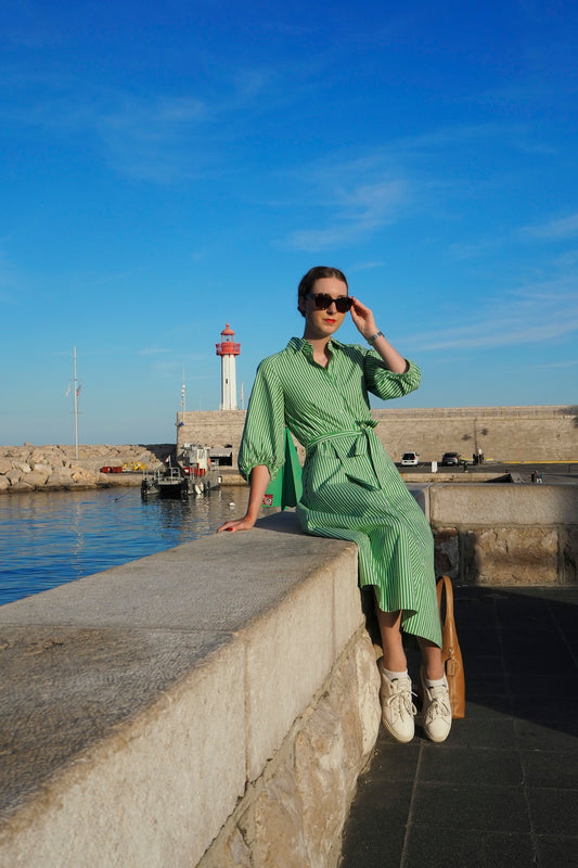 Woman in green dress sitting by a harbor lighthouse.