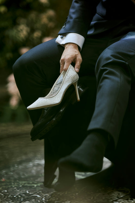 Person in suit holds elegant white high-heeled shoe.