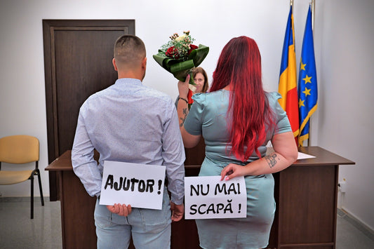 A man and a woman holding signs reading AJUTOR and NU MAI SCAPĂ